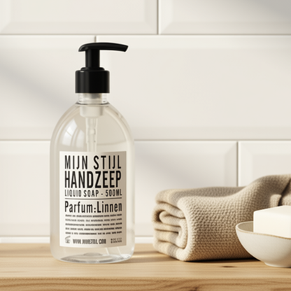 Mijn Stijl handzeep Linnen (500 ml) in een transparante fles met zwart pompje, geplaatst op een houten ondergrond. Rechts naast de fles ligt een opgerolde of gevouwen handdoek met een grove wafelstructuur, tegen een achtergrond van een lichte, betegelde wand.